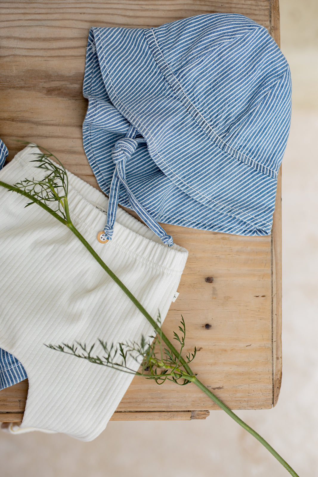 1+ in the family Marti off-white drapiert auf einem Tisch mit einer jeansblauen Mütze, Blick von oben 