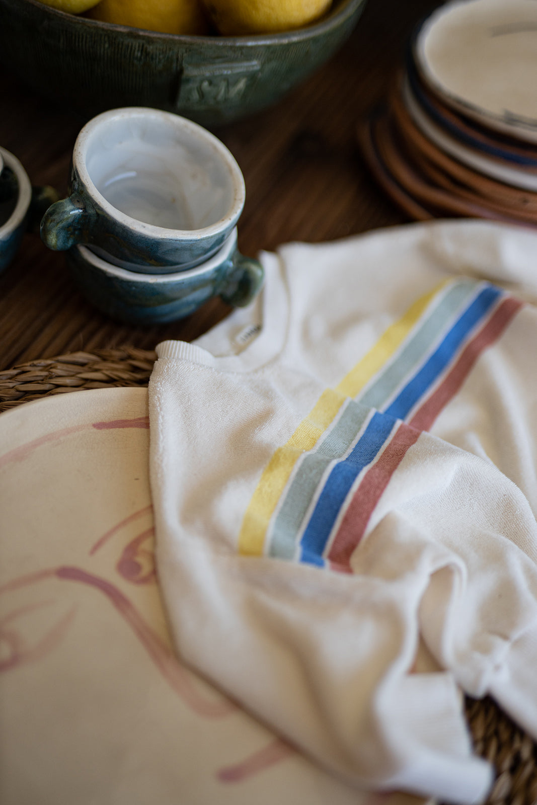 1+ in the family Santanyi off-white Produktbild drapiert auf einem Tisch mit Blick auf die bunten Querstreifen 