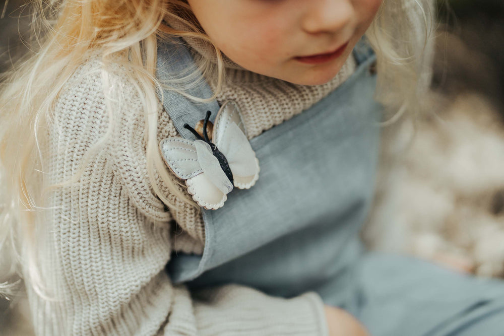 Donsje Alja Clip Vlinder silver grey metallic leather getragen von einem Mädchen, angesteckt an ihrem Latzhosenträger, Ansicht von vorne