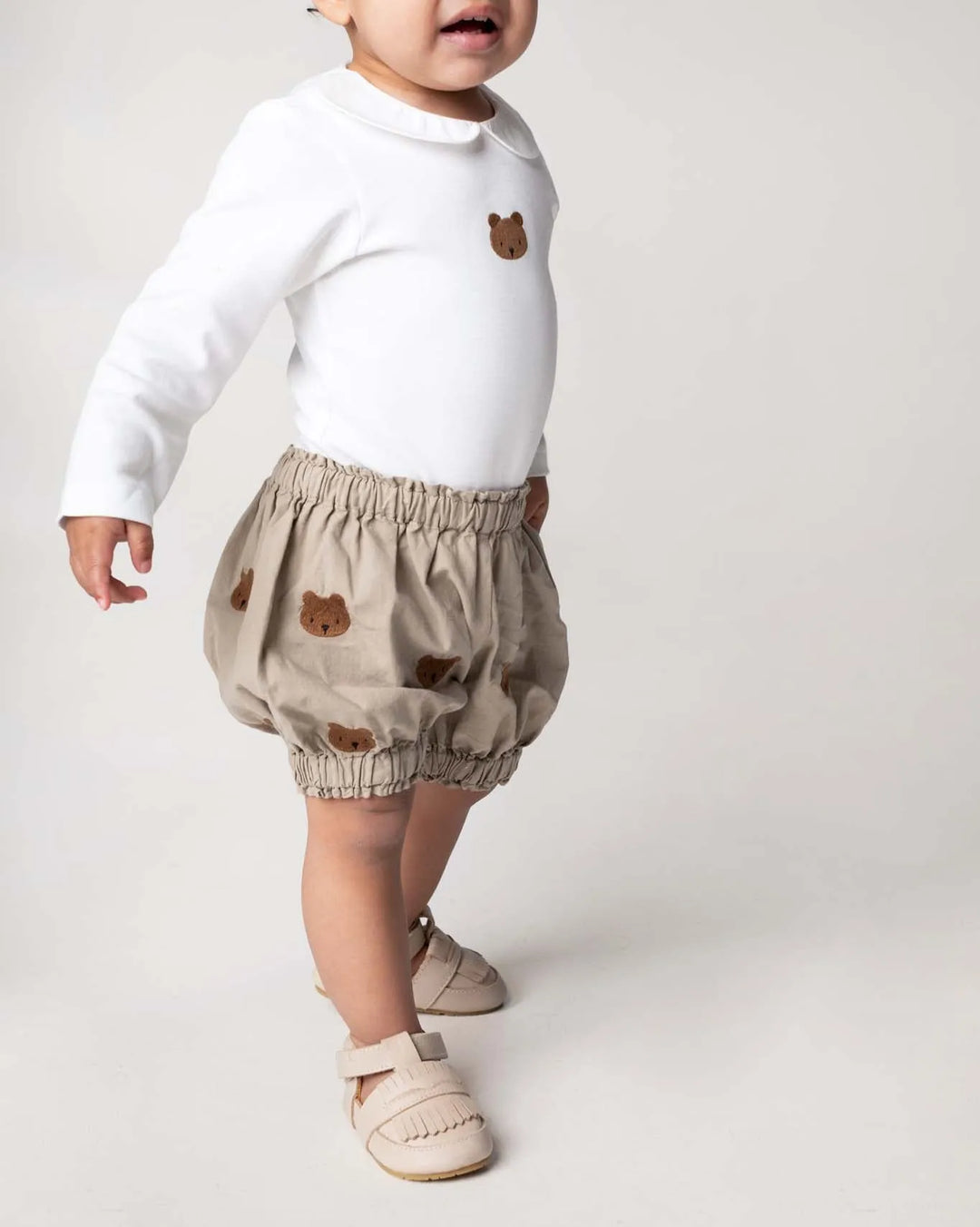 Donsje Carson Bloomers Bears dusty green getragen von einem Kleinkind vor weißem Hintergrund, Ansicht seitlich frontal mit Blick auf die aufgestickten Bären