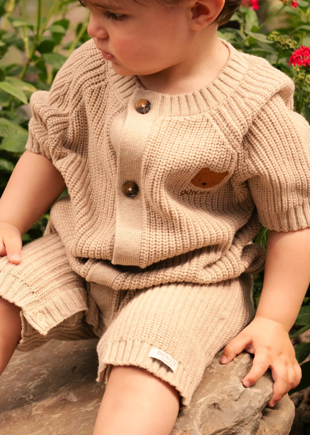 Donsje Dantje Jumpsuit Bear milk chocolate getragen von einem sitzenden Kleinkind Ansicht von vorne