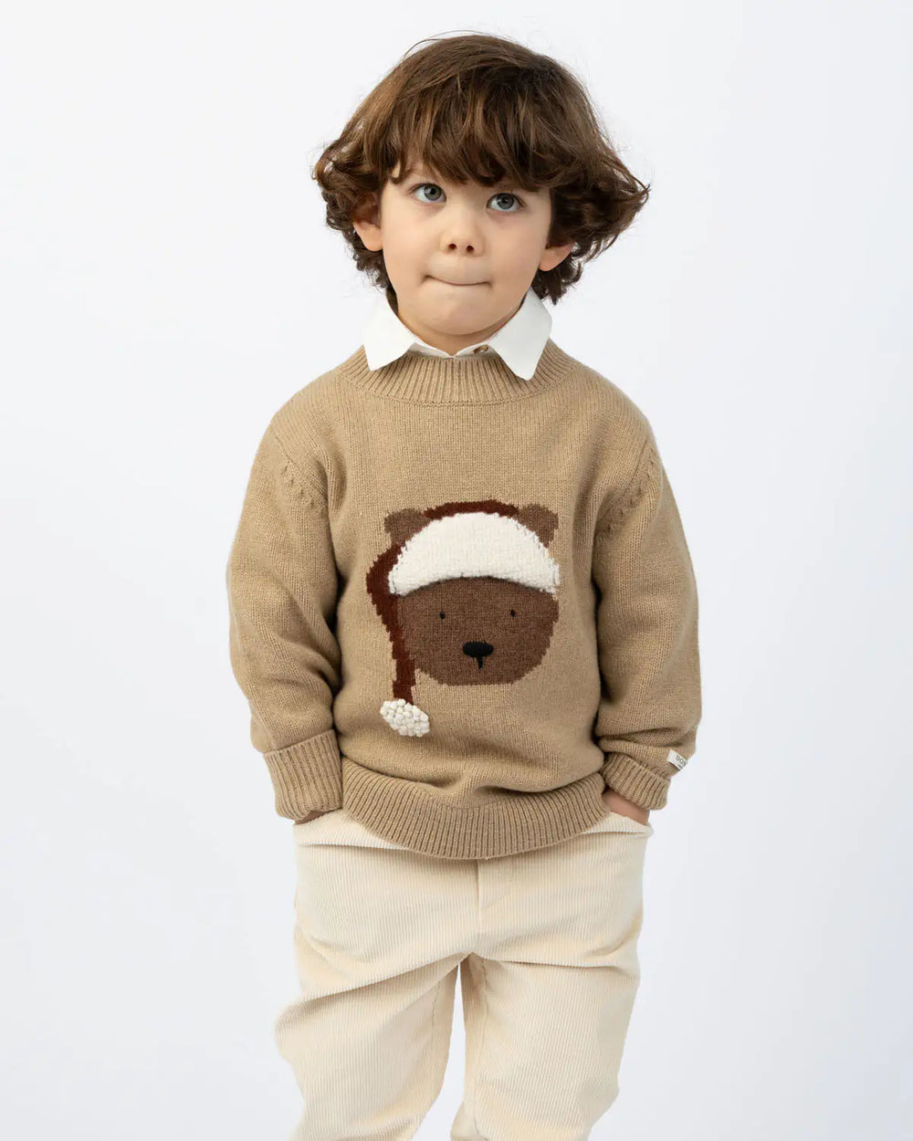 Donsje Denn Merino Wool Sweater Christmas Bear latte melange getragen von einem Jungen vor einer weißen Leinwand stehend, Ansicht von vorne. 
