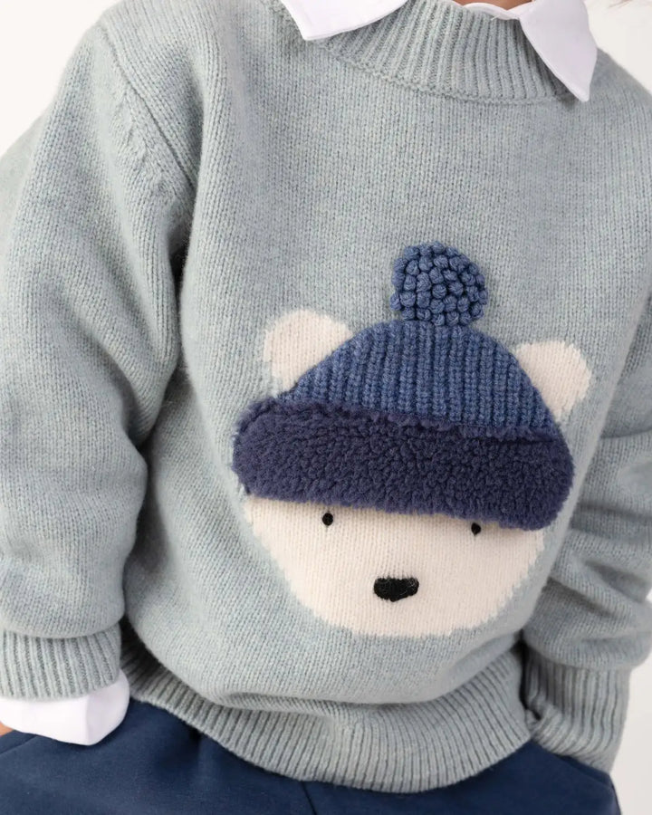 Donsje Denn Merino Wool Sweater Polar Bear cloud blue melange getragen von einem Kind, Detailansicht Eisbären-Gesicht mit Pudelmütze. 