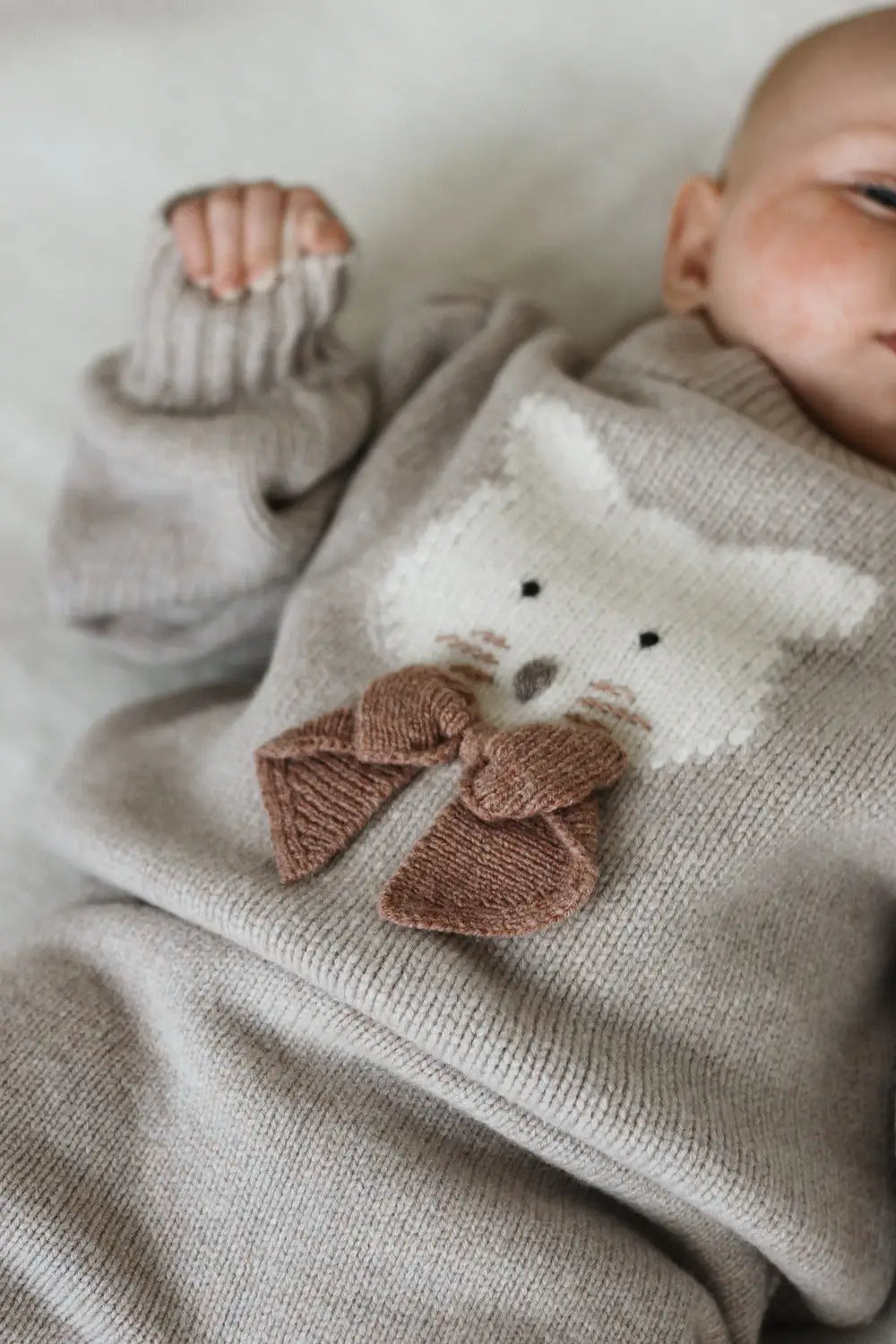 Donsje Denna Merino Wool Sweater Cat ash rose getragen von einem Baby auf dem Rücken liegend, Ansicht von oben. 