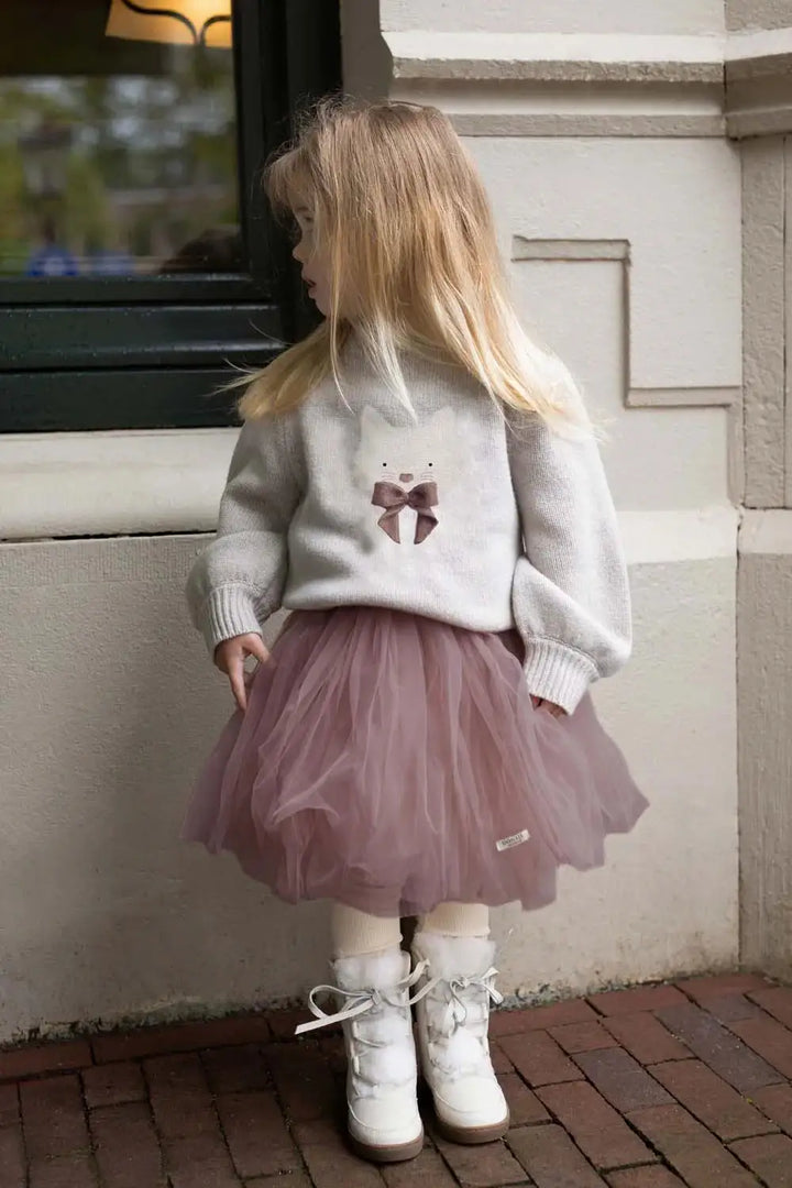 Donsje Denna Merino Wool Sweater Cat ash rose getragen von einem Mädchen vor einer Hauswand stehend. Ansicht von vorne. 