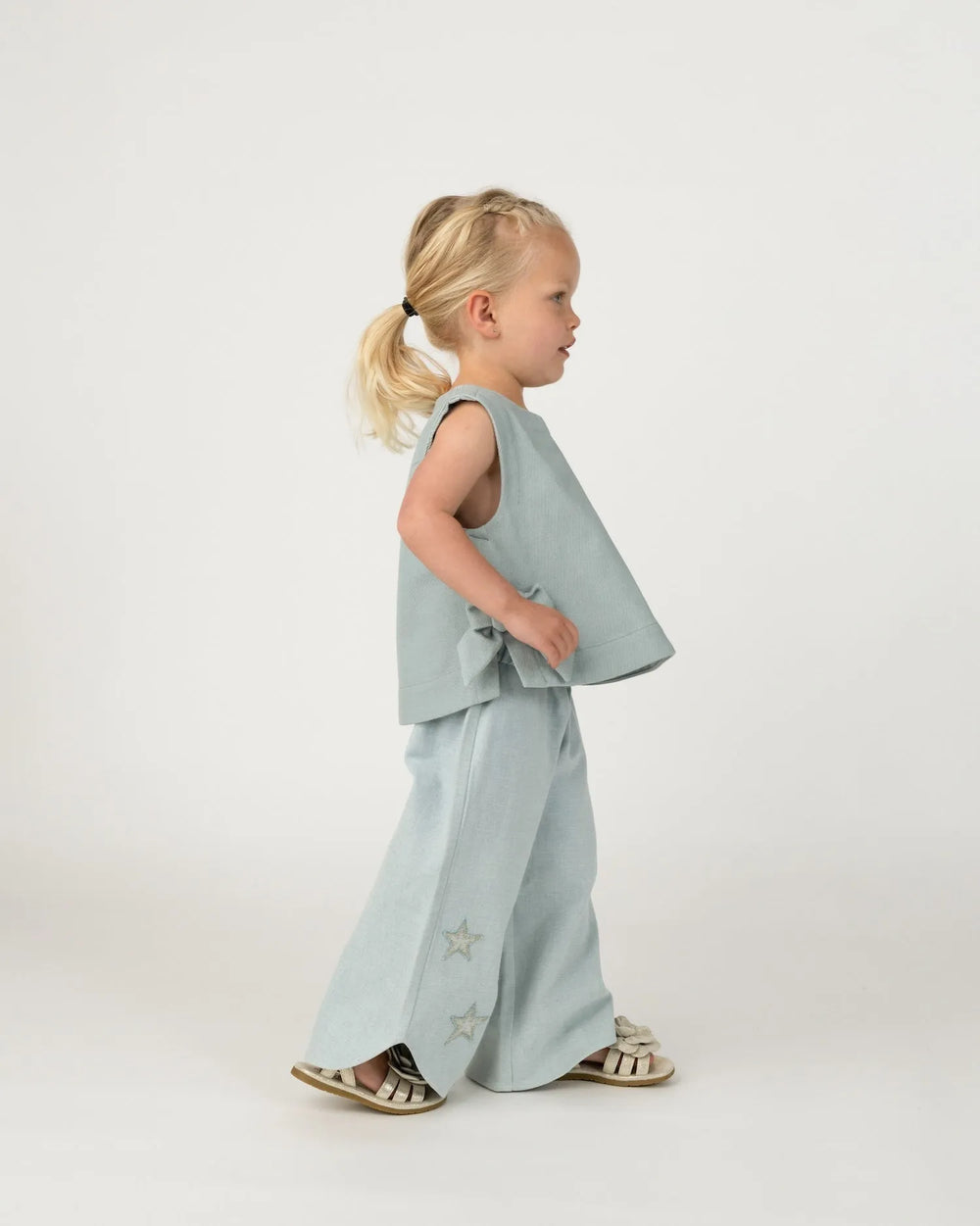 Donsje Hauke Denim Trousers Stars ice blue getragen von einem Mädchen vor weißem Hintergrund Ansicht von der Seite mit Blick auf die Sternenstickerei und das weite Bein