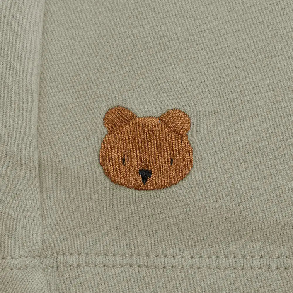 Donsje Ithri Shorts Bear dusty green Detailaufnahme aufgesticktes Donsje Bärengesicht auf grau-grünem Baumwollstoff