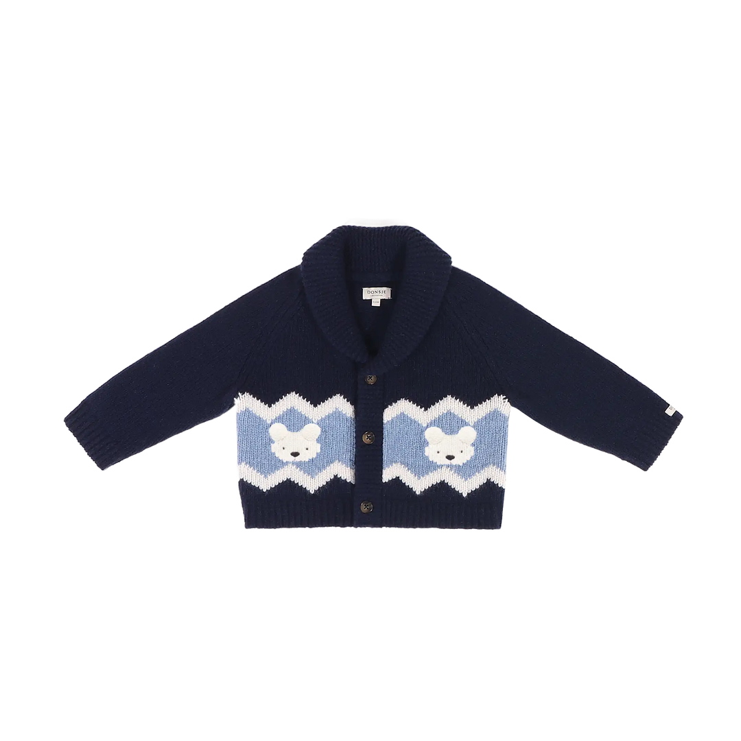 dunkelblaue Strickjacke für Kinder aus 100% Merinowolle mit elegant aussehendem umgeschlagenen Kragen, durchgehender Knopfleiste und einem hellblauen-weißen Streifen oberhalb des unteren Saums, in welchen weiße Eisbären-Gesichter eingestrickt sind. Produktbild, Ansicht von vorne. 