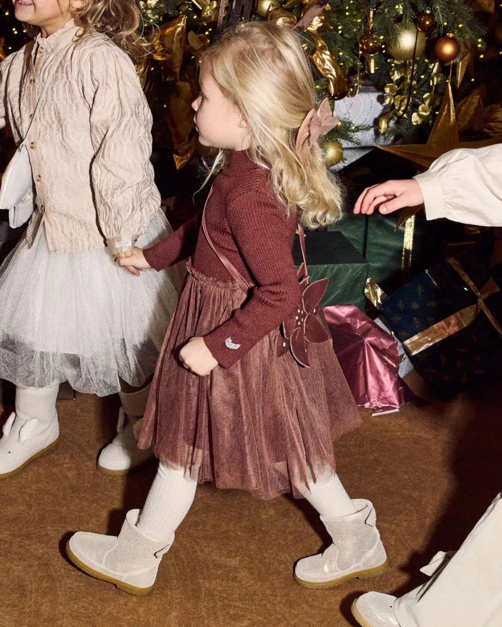Donsje Lotus Dress Rustic Brown getragen von einem Mädchen vor einem Weihnachtsbaum, Ansicht von vorne. 