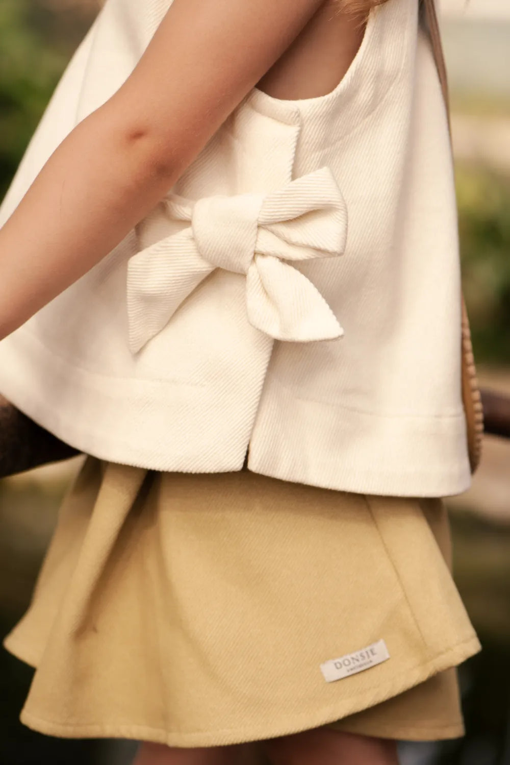 Donsje Veeri Top birch getragen von einem Mädchen, Ansicht von der Seite mit Fokus auf die seitlich angebrachte Schleife