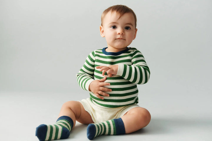 FUB Baby Rib Blouse ecru pine getragen von einem Baby sitzend vor weißem Hintergrund, kombiniert mit den Classic Stripe Socks in pine/ocean