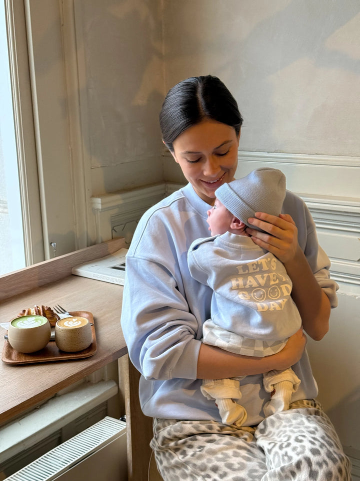 Famvibes GOOD DAY Sweatshirt Baby pastell-blue getragen von einem Neugeborenen auf dem Arm seiner Mutter