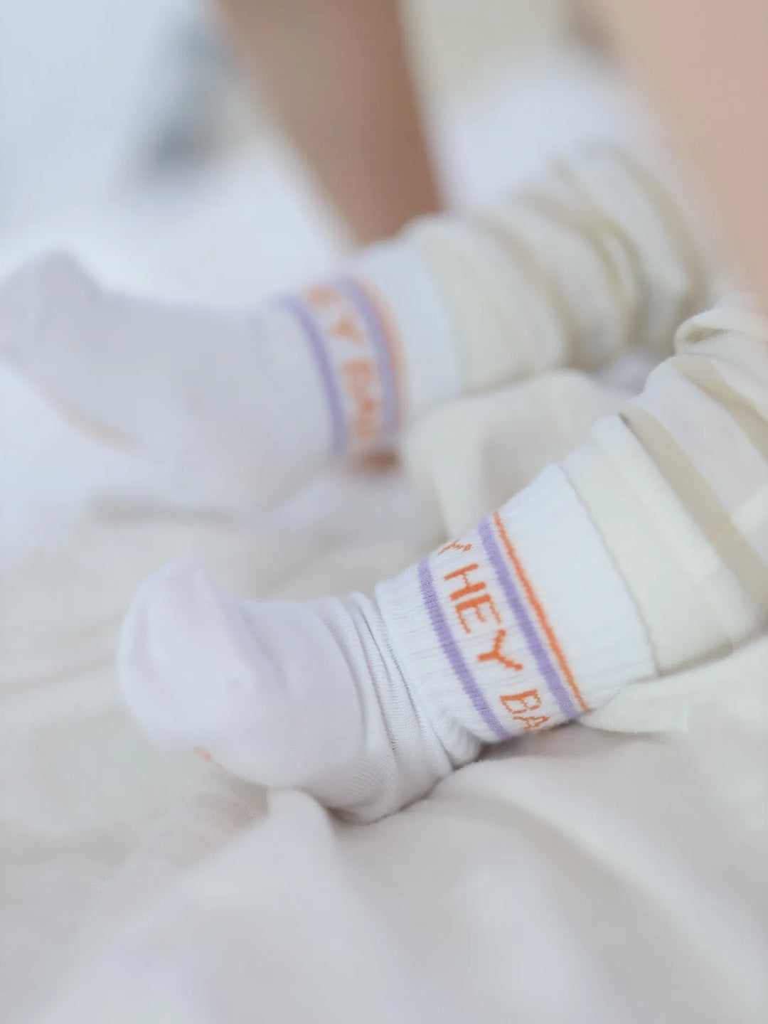weiße Socken für Babys aus Baumwolle mit lila-orangefarbenem Schriftzug Hey Baby