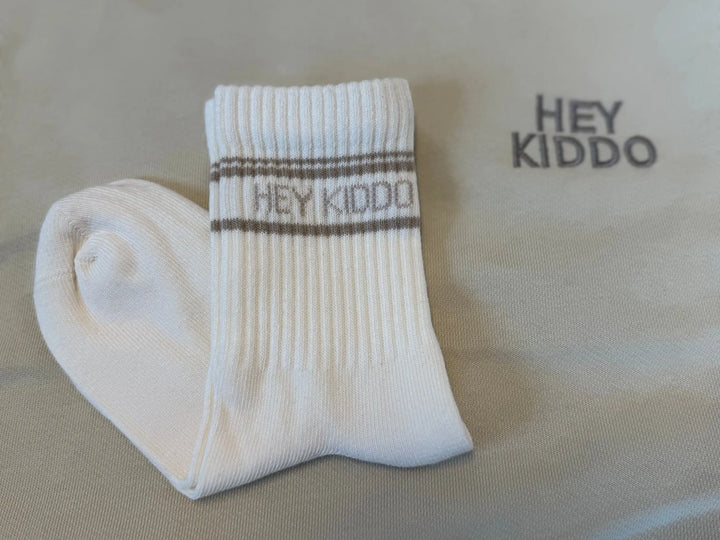 weiße Socken für Kinder aus Baumwolle mit taupefarbenem Schriftzug Hey Kiddo