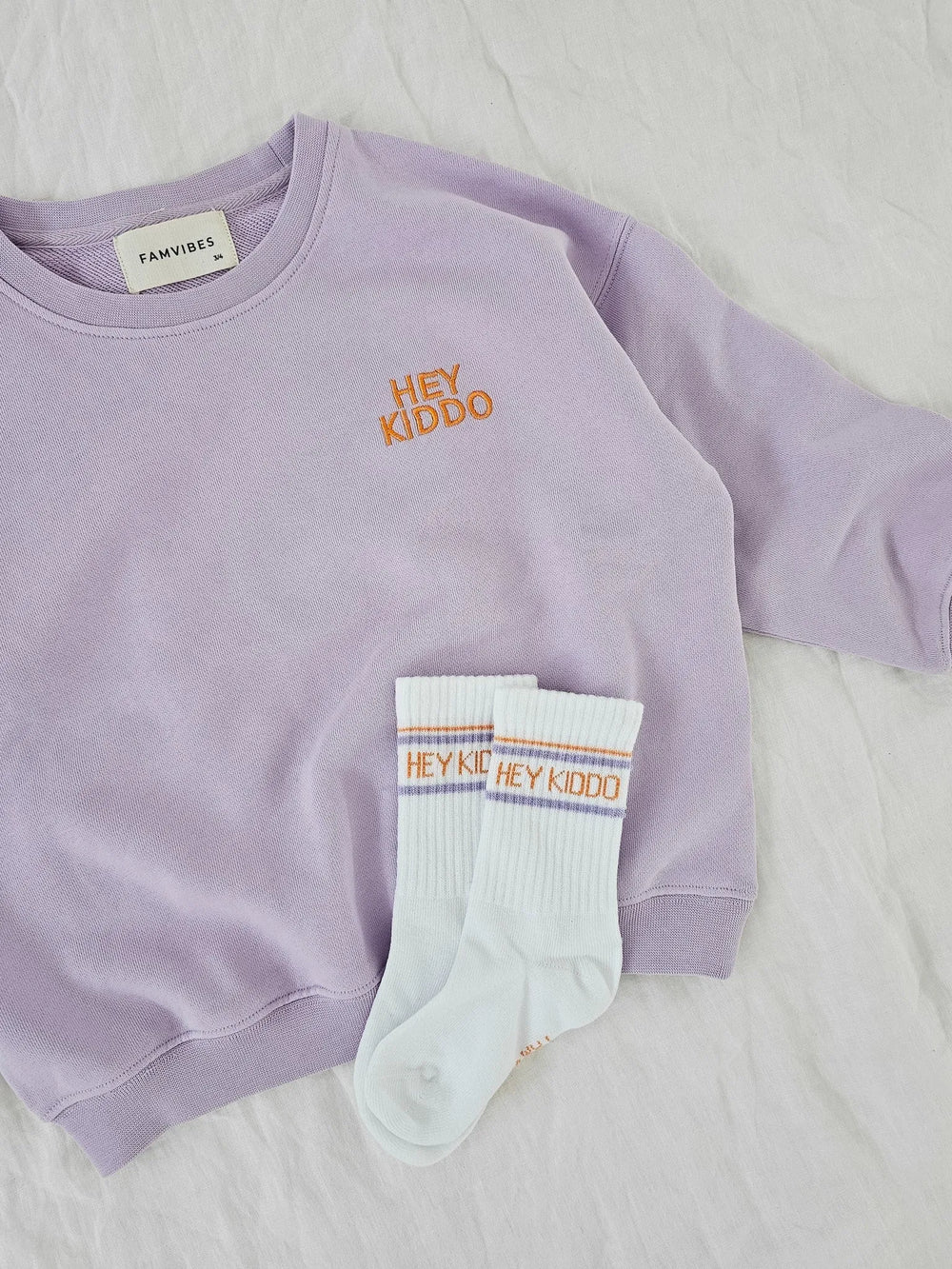 weiße Socken für Kinder aus Baumwolle mit lila- und orangefarbenem Schriftzug Hey Kiddo
