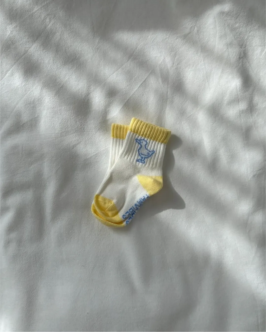 weiße Socken für Babys aus Baumwolle mit gelben Akzenten an der Fußspitze, der Hacke und dem Bündchen und hellblauer Ente am Knöchel