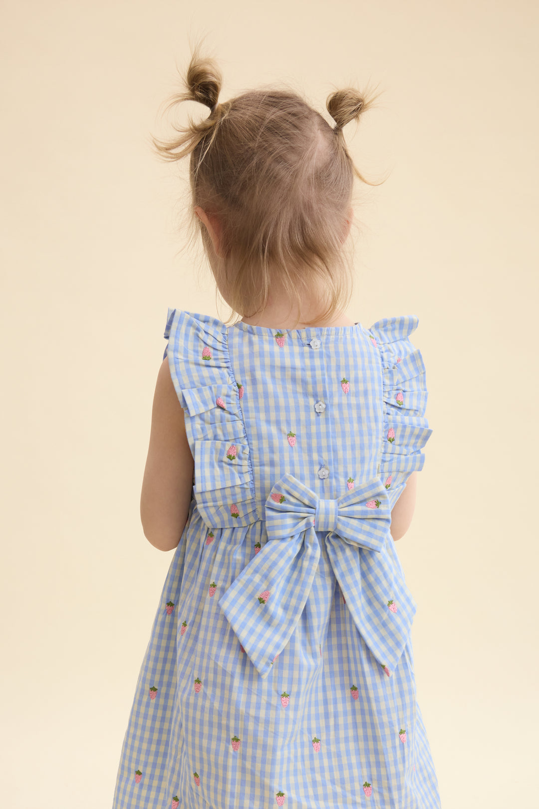 hellblau weiß kariertes, ärmelloses Kleid für Mädchen aus 100% Baumwolle mit kleinen aufgestickten Erdbeeren in rosa. Rüschen an den Schultern, Schleife und Blümchen Knöpfe am Rücken