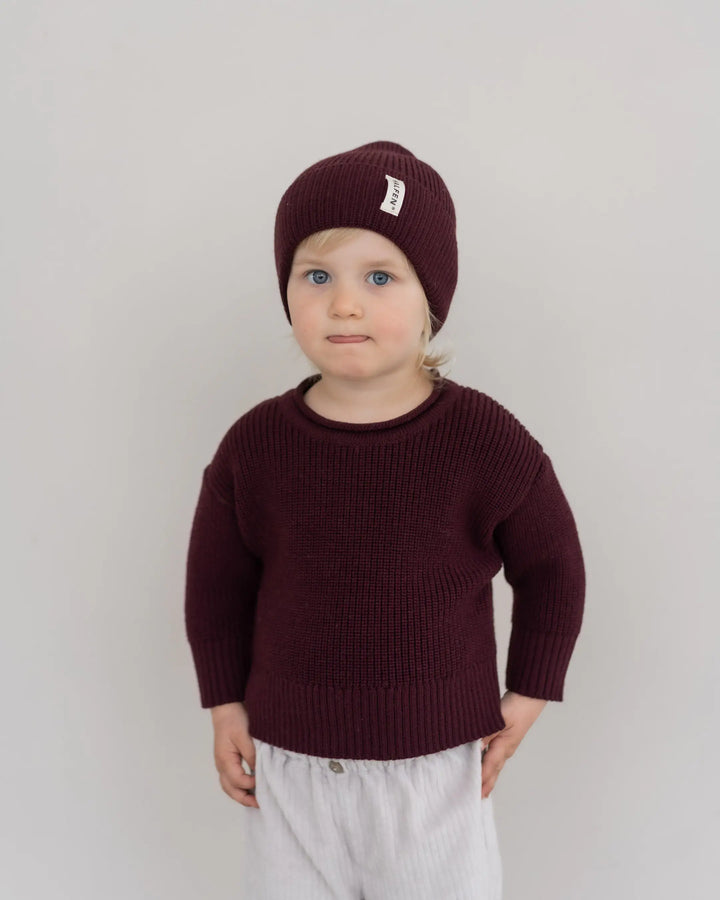 Halfen Strick-Beanie Merino cherry getragen von einem Kind vor beigefarbener Leinwand, Ansicht von vorne. 