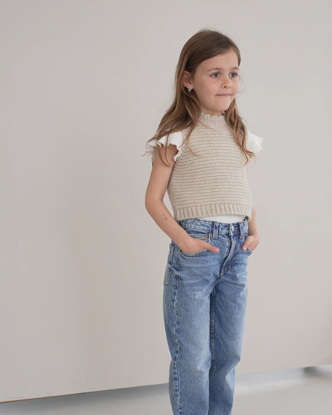 Halfen Struktur Pullunder Alpaca K7S35 beige getragen von einem Mädchen vor einer Leinwand stehend, Ansicht von der Seite vorne. 