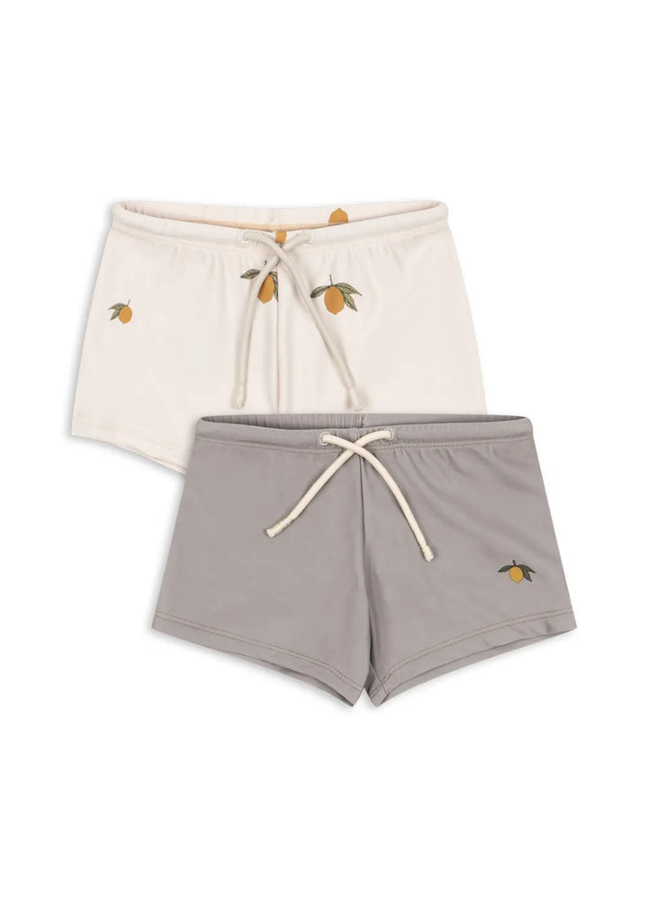 Doppelpack Badehosen für Jungen im Radlerhosenstil. Eine cremefarben mit Allover-Zitronenprint, eine hellgrau mit einer aufgedruckten Zitrone am unteren linken Bein. Jeweils mit Gummibund und Fixier-Schnur. 