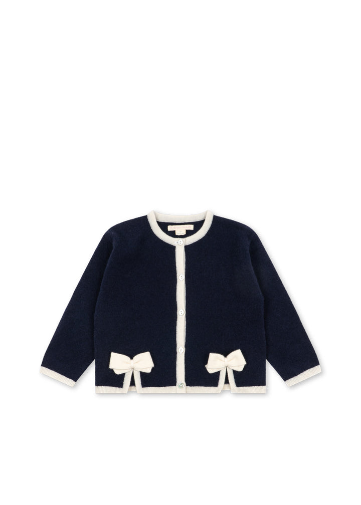 Dunkelblauer Cardigan für Mädchen aus 100% Wolle mit weißen Nähten am Rundhalsausschnitt, an der durchgehenden Knopfleiste und am Saum sowie an den Ärmelenden. Mit zwei weißen Schleifen oberhalb des unteren Saums. Produktbild, Ansicht von vorne. 