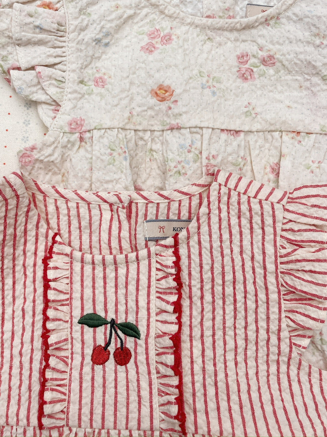 Konges Sloejd Ellie Frill Romper GOTS amour stripe drapiert mit einem anderen Strampler, Blick auf Rundhalsausschnitt und aufgestickte Kirsche