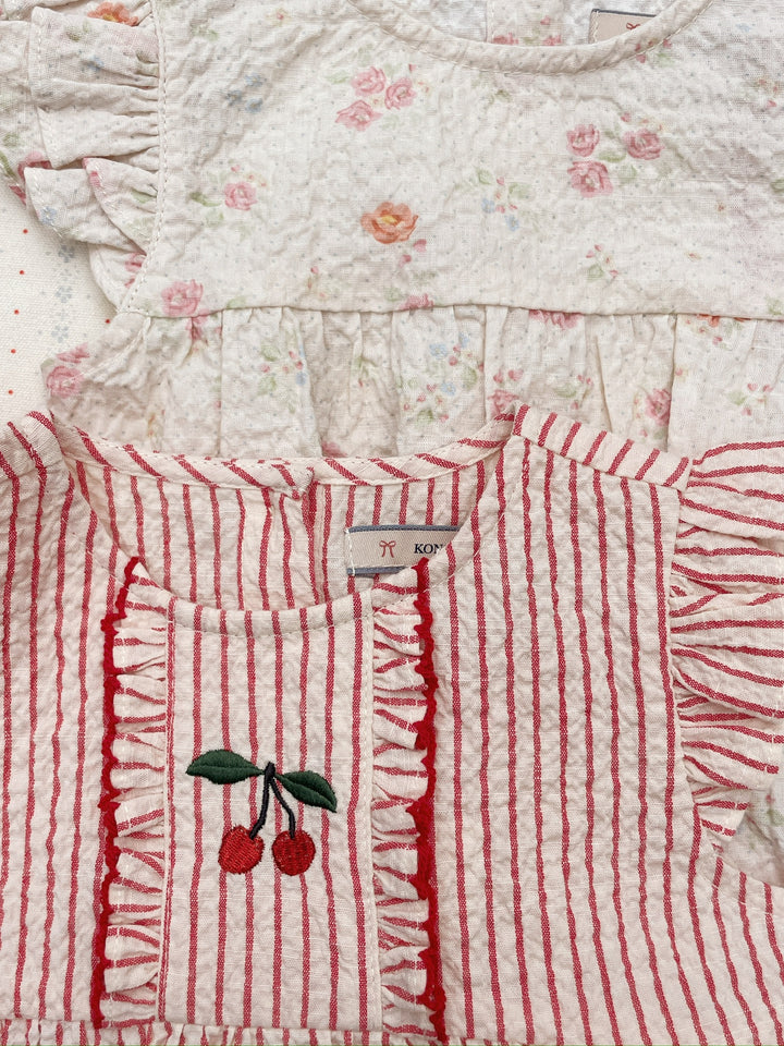 Konges Sloejd Ellie Frill Romper GOTS amour stripe drapiert mit einem anderen Strampler, Blick auf Rundhalsausschnitt und aufgestickte Kirsche