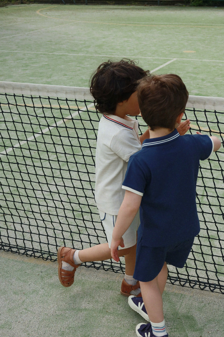 Konges Sloejd Florian Shorts spellbound getragen von einem Jungen auf einem Tennisplatz, Ansicht von hinten 