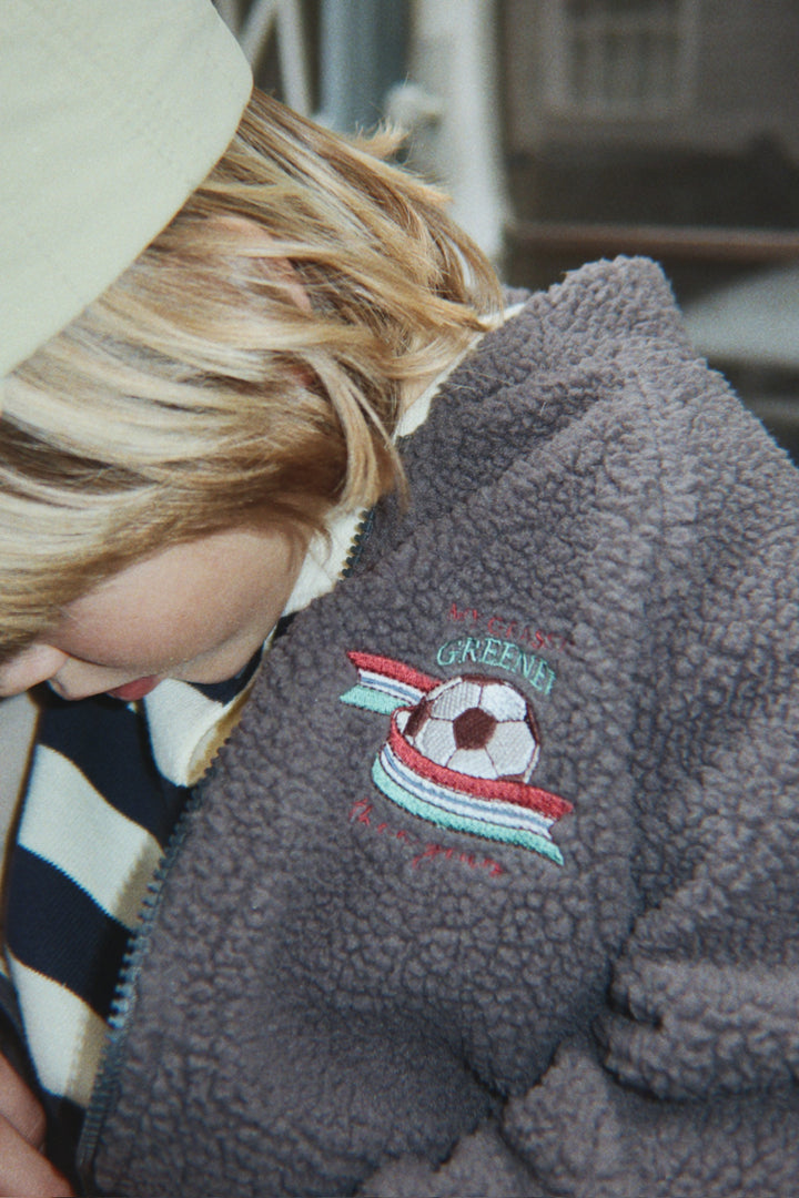 Konges Sloejd Jody Bomber Jacket GRS magnet getragen von einem Jungen, Detailansicht kleiner aufgestickter Fußball auf der Vorderseite auf Höhe der linken Brust. 