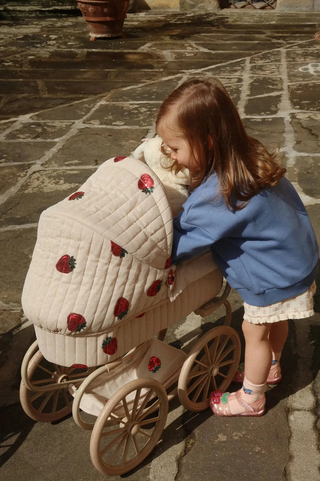 Konges Sloejd Loumilla Sweat Shirt OCS colony blue getragen von einem kleinen Mädchen, das sich über einen Puppenwagen beugt, Ansicht von der Seite