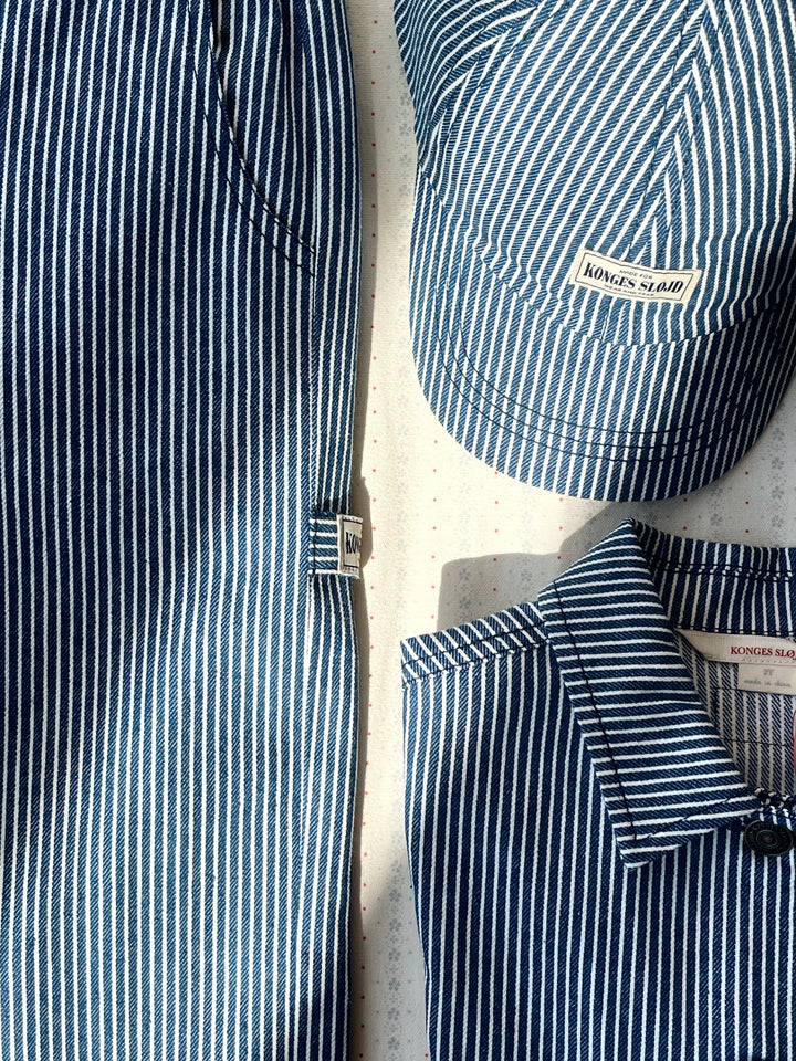 Konges Sloejd Luc Pants GOTS blue stripe drapiert mit farbgleichem Hemd und Cap.