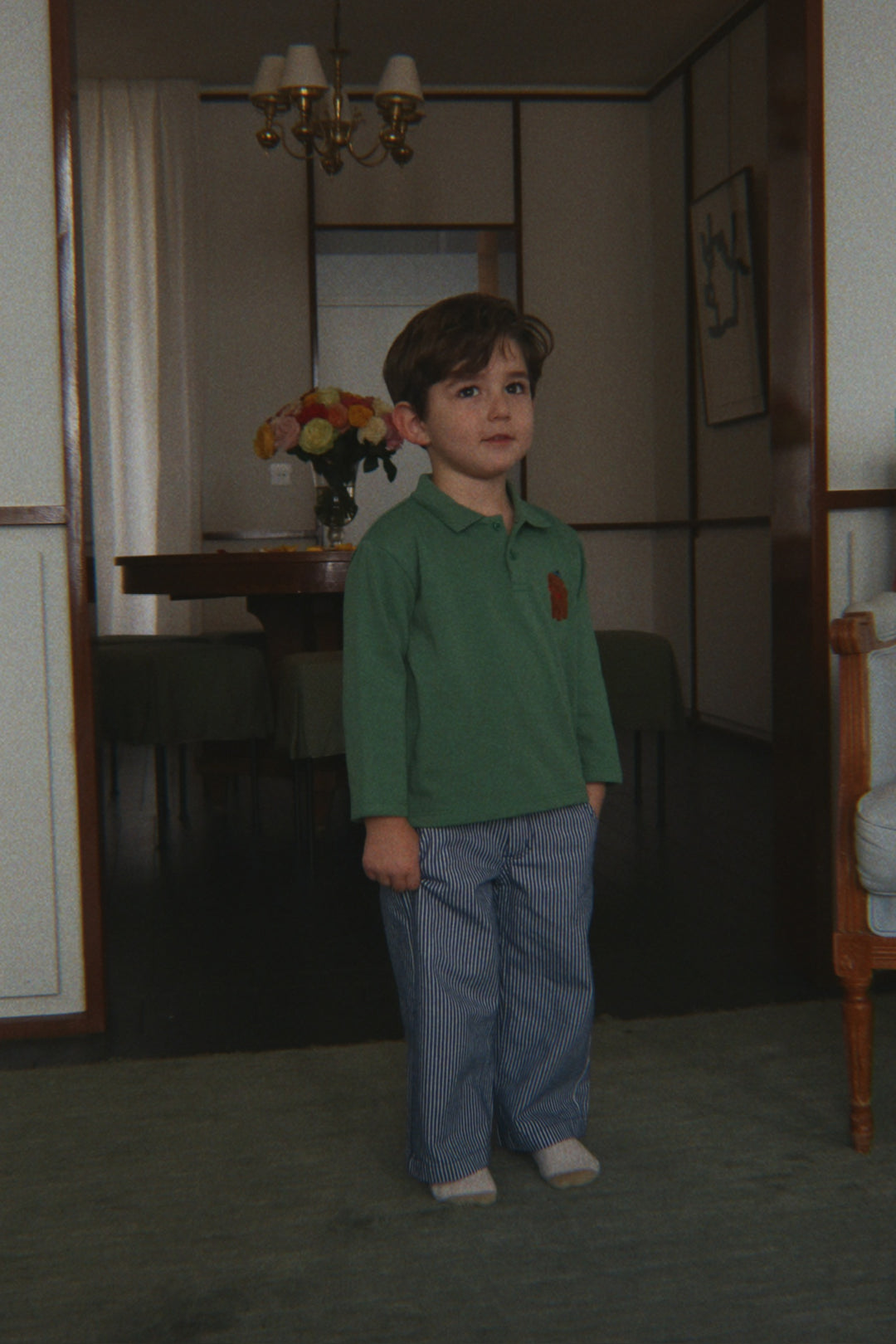 Konges Sloejd Luc Pants GOTS blue stripe getragen von einem Kind in einem Türrahmen stehend, Ansicht von vorne. 