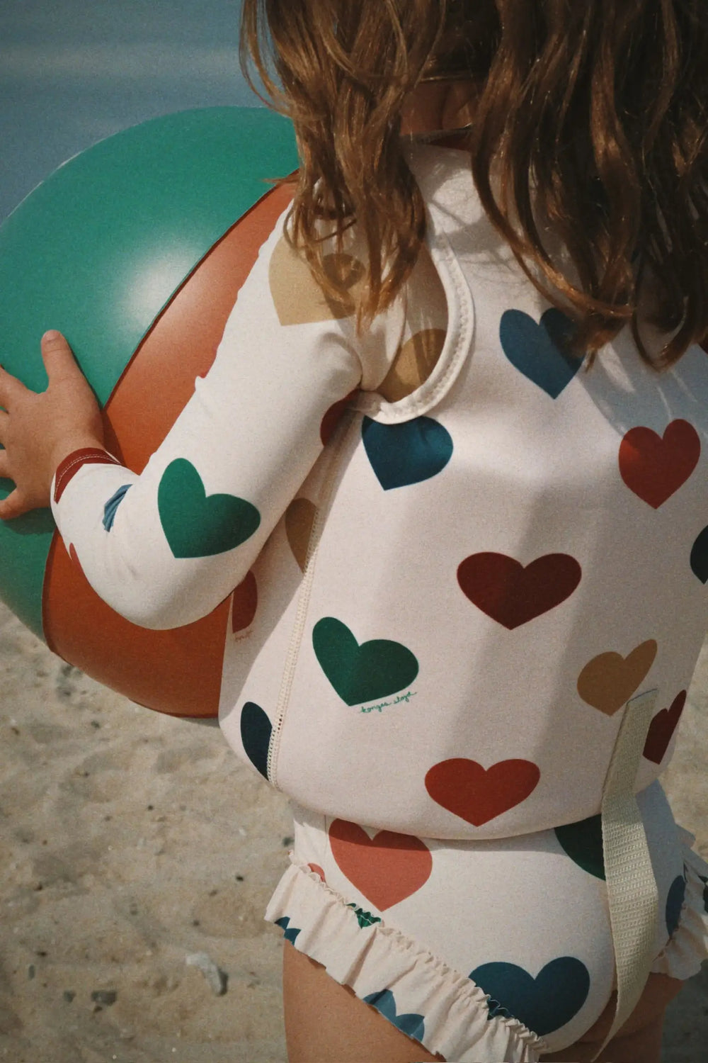Konges Sloejd Manuca LS Swimsuit GRS bon coeur coloré getragen von einem Mädchen am Strand, Ansicht der Rückseite. 