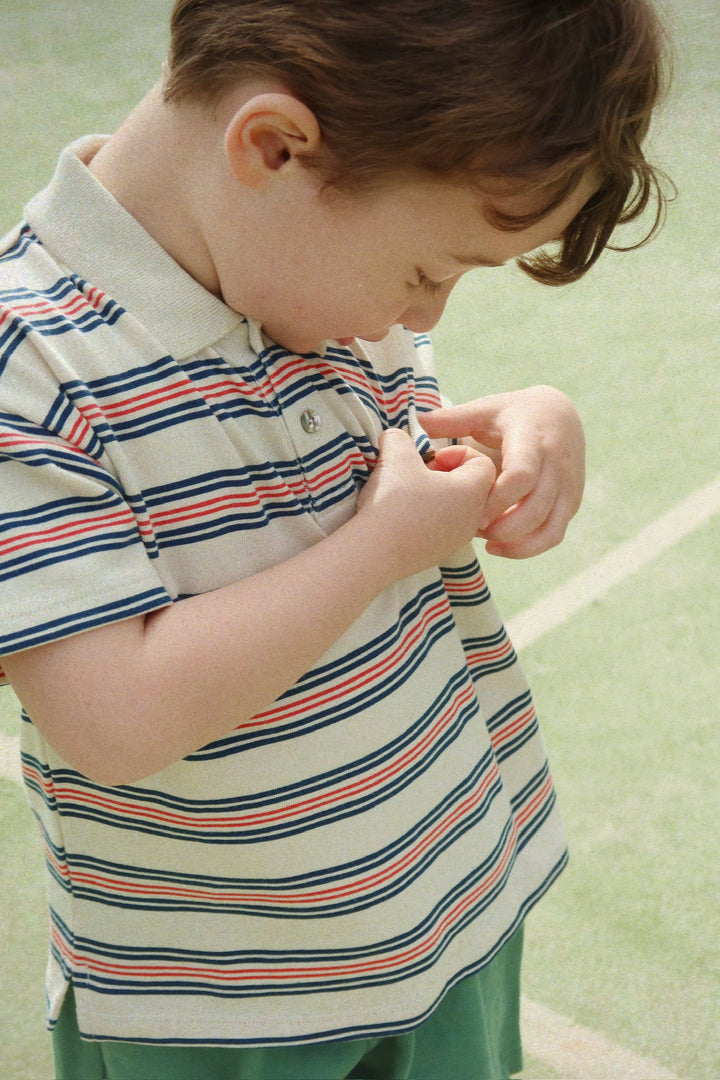 Konges Sloejd Spotty SS Polo stripie stripe getragen von einem Jungen auf einem Tennisplatz, Ansicht von der Seite 