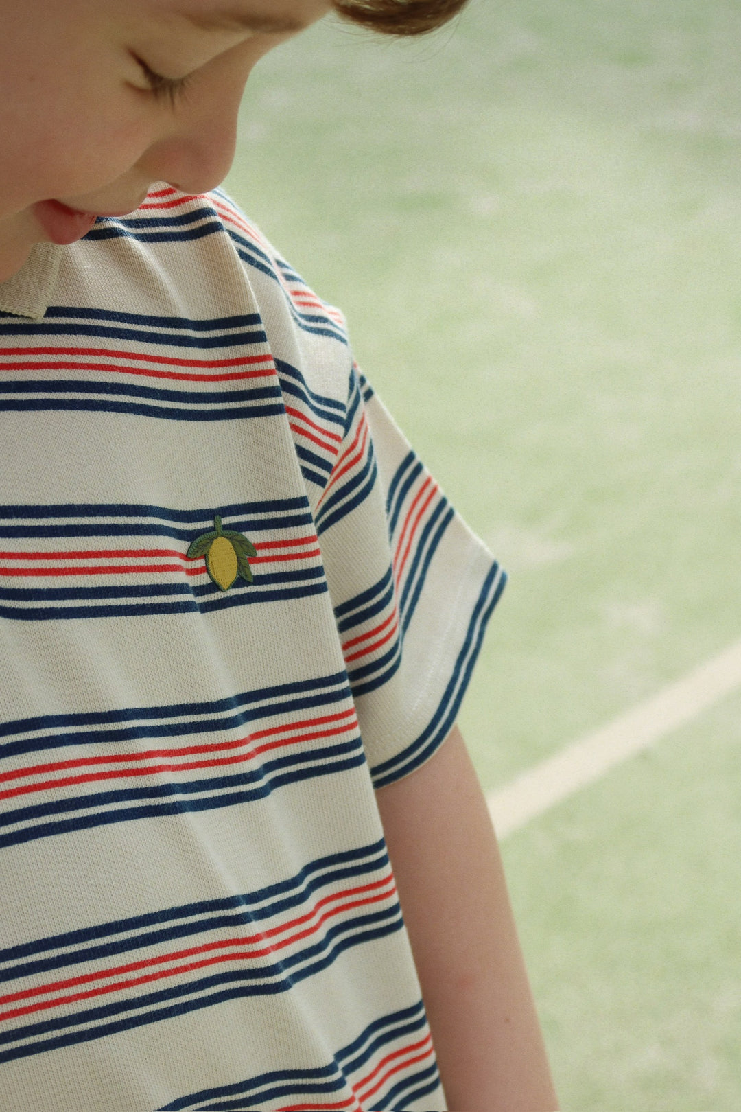 Konges Sloejd Spotty SS Polo stripie stripe  getragen von einem Jungen auf einem Tennisplatz, Nahaufnahme aufgestickte Zitrone