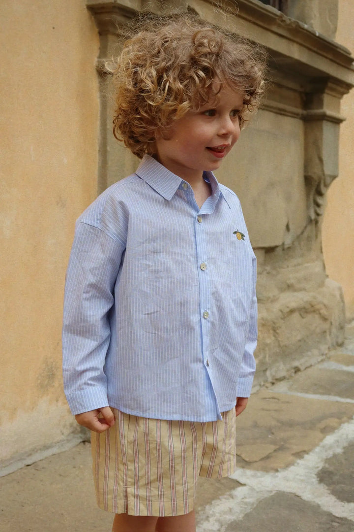 Konges Sloejd Wes Shirt GOTS blue stripe getragen von einem männlichen Kleinkind vor einer gelben Gebäudemauer Ansicht von vorne