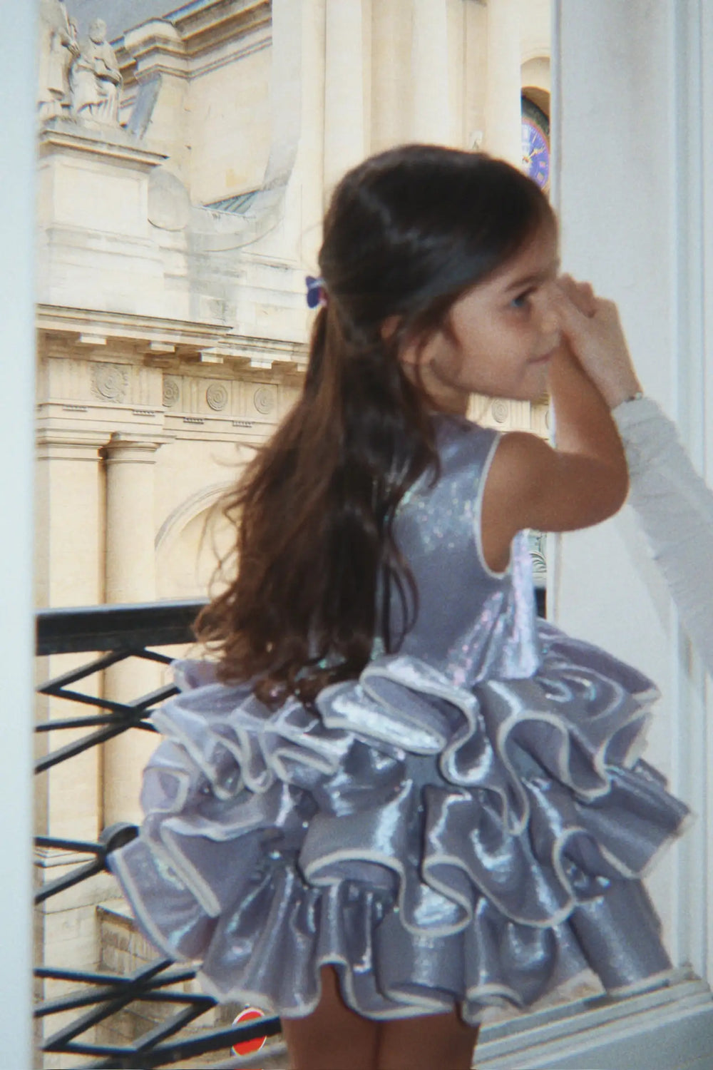 Konges Slojd Fia Frill Dress GRS sleet getragen von einem kleinen Mädchen vor einem Fenster stehend. 