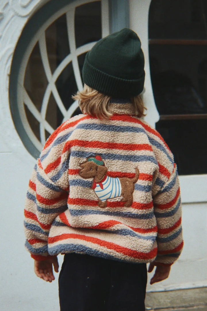 Konges Slojd Jody Embroidery Teddy Jacket GRS tangerine stripe getragen von einem Kind vor einer Hauswand stehend, Ansicht der Rückseite mit großem Dackel-Aufnäher. 