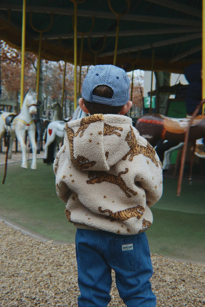 Konges Slojd Jody Teddy Hoodie GRS tiger getragen von einem Jungen vor einem Karussell stehend, Ansicht der Rückseite. 