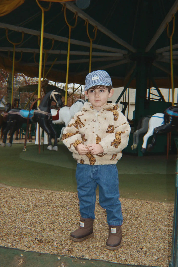 Konges Slojd Jody Teddy Hoodie GRS tigergetragen von einem kleinen Jungen vor einem Karussell stehend, Ansicht von vorne. 