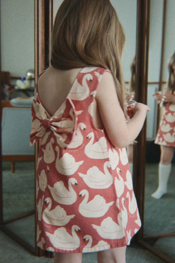 Konges Slojd Magot Bow Dress GOTS swan rose getragen von einem kleinen Mädchen vor einem Spiegel stehend, Ansicht der Rückseite. 