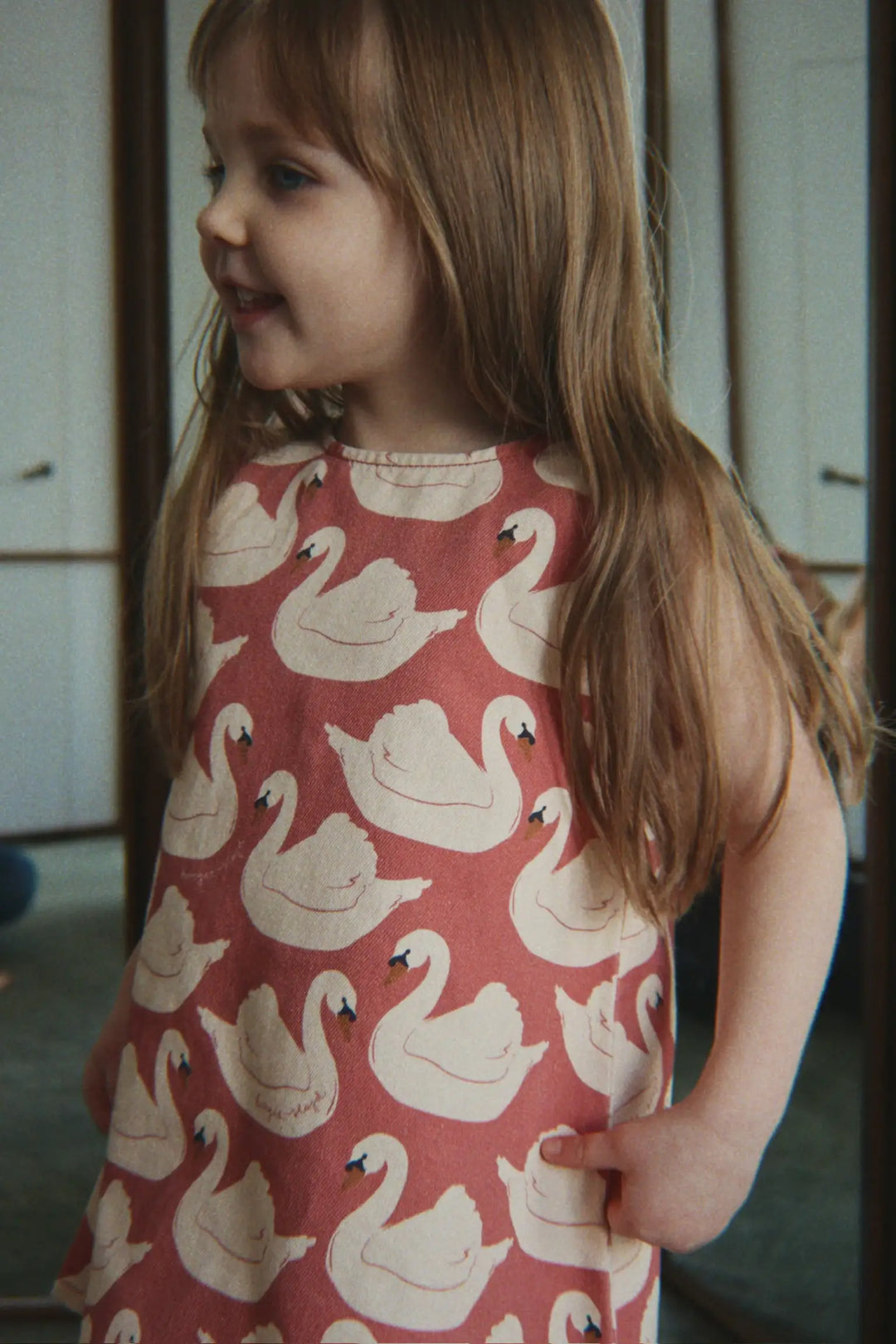 Konges Slojd Magot Bow Dress GOTS swan rose getragen von einem kleinen Mädchen vor einem Spiegel stehend, Ansicht von vorne. 