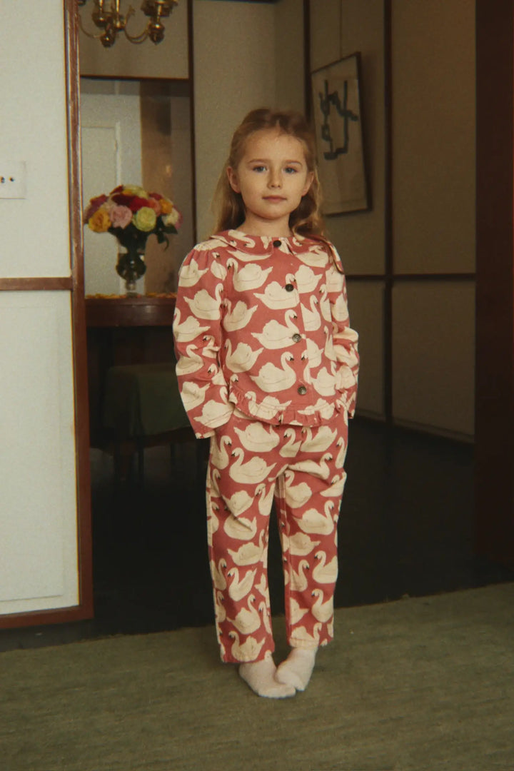 Konges Slojd Magot Frill Pants GOTS swan rose getragen von einem kleinen Mädchen in einem Türrahmen stehend, Ansicht von vorne. 