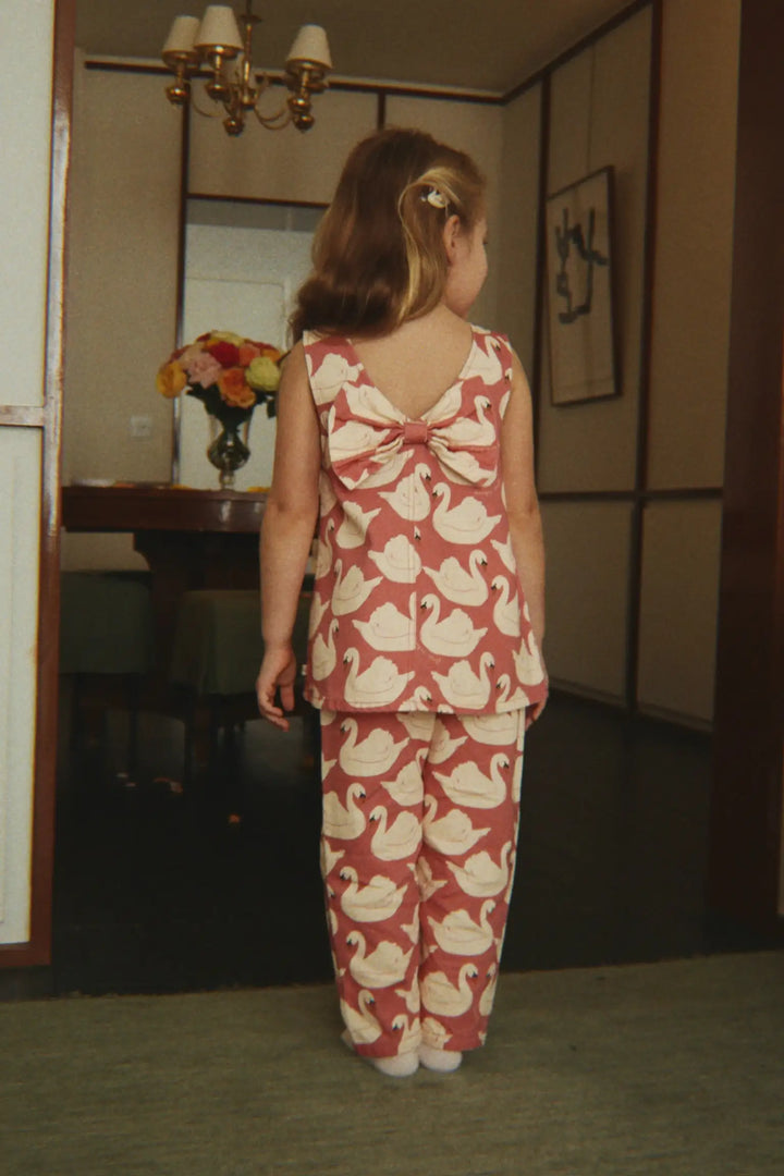 Konges Slojd Magot Frill Pants GOTS swan rose getragen von einem kleinen Mädchen in einem Türrahmen stehend, Ansicht der Rückseite. 