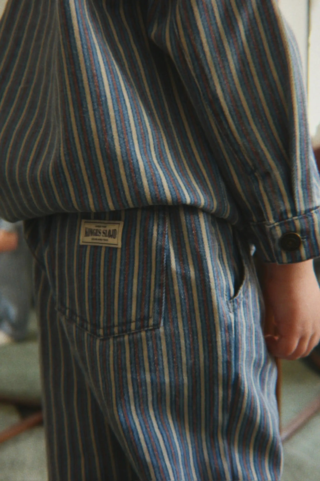 Konges Slojd Magot Pants GOTS tricolore bleu getragen von einem Kind, Ansicht von der Seite mit Blick auf die Gesäßtasche mit aufgenähtem Konges Sløjd Label. 