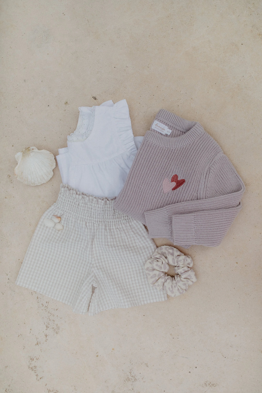 Leevje Chunky Knit Pullover hearts lavender auf beigefarbenem Boden liegend, drapiert mit passender Hose und Bluse