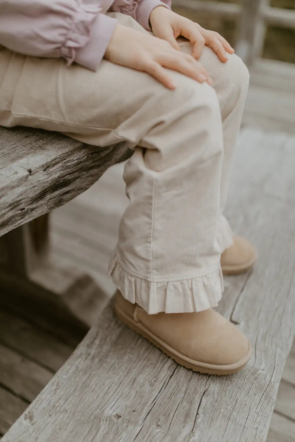 beigefarbene Cordhose aus Baumwolle und Elasthan für Mädchen mit geradem Bein, Rüschen am Saum der Fußenden und mit breitem bequemem Gummibund. Getragen von einem Kind, Detailansicht Rüschen am Fußende. 
