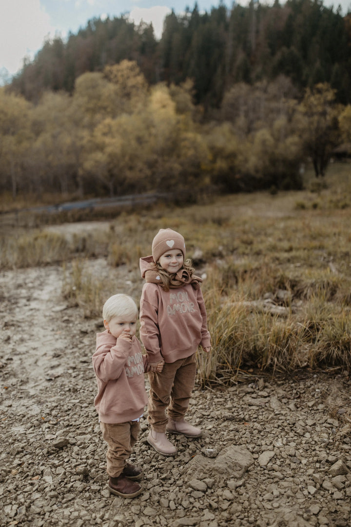 Leevje Corduroy Pants pecan getragen von einem Mädchen und einem Jungen auf einer Wiese stehend, Ansicht von vorne. 