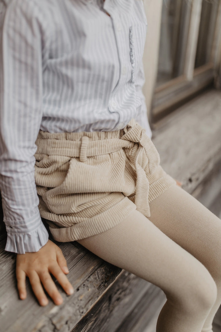 Leevje Corduroy Shorts dusty rose getragen von einem Mädchen auf einer Fensterbank sitzend, Ansicht von der Seite. 