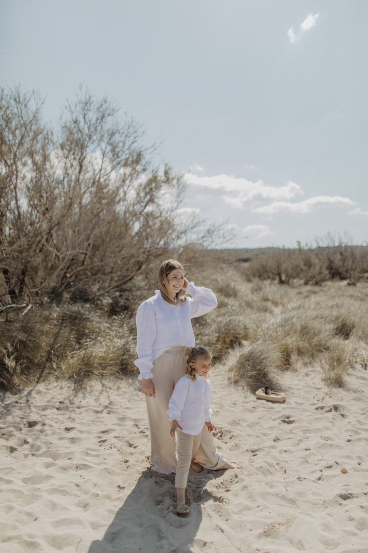 Leevje Mini-Me Muslin Blouse white getragen von einer Dame und einem Mädchen im Mini-Me Partnerlook am Strand stehend, Ansicht von vorne. 
